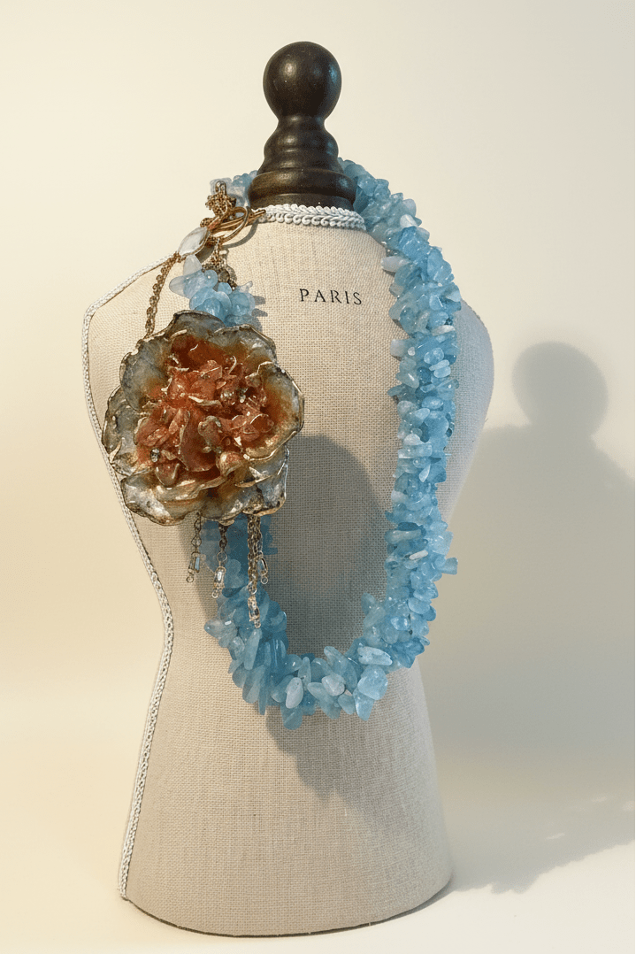 Collar aguamarina flor terracota — editorial fondo crema