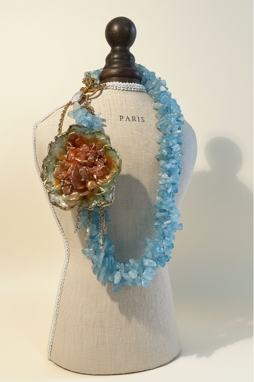 Collar aguamarina flor terracota — editorial fondo crema